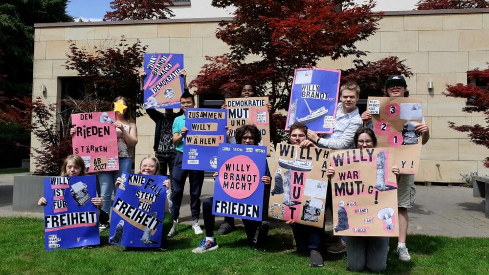 Gruppenbild mit Jugendlichen, die ihre selbstgemachten Ausstellungsplakate hochhalten